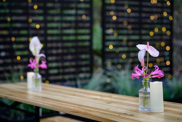 Communal tables set with candles and bud vases in front of string-lit panels