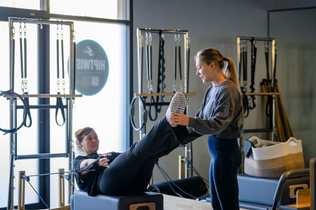 An instructor helps a guest try a reformer