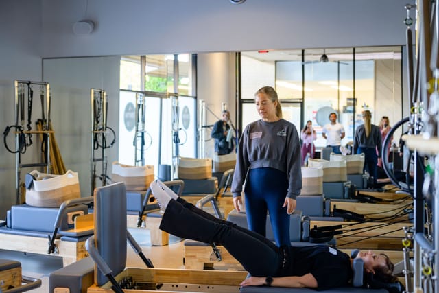 An instructor guides a guest on the reformer