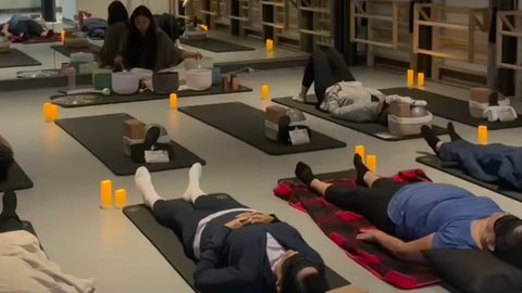 Members lying in savasana on mats by candlelight while an instructor plays crystal singing bowls at Hiptwist Fitness Studio, San Mateo